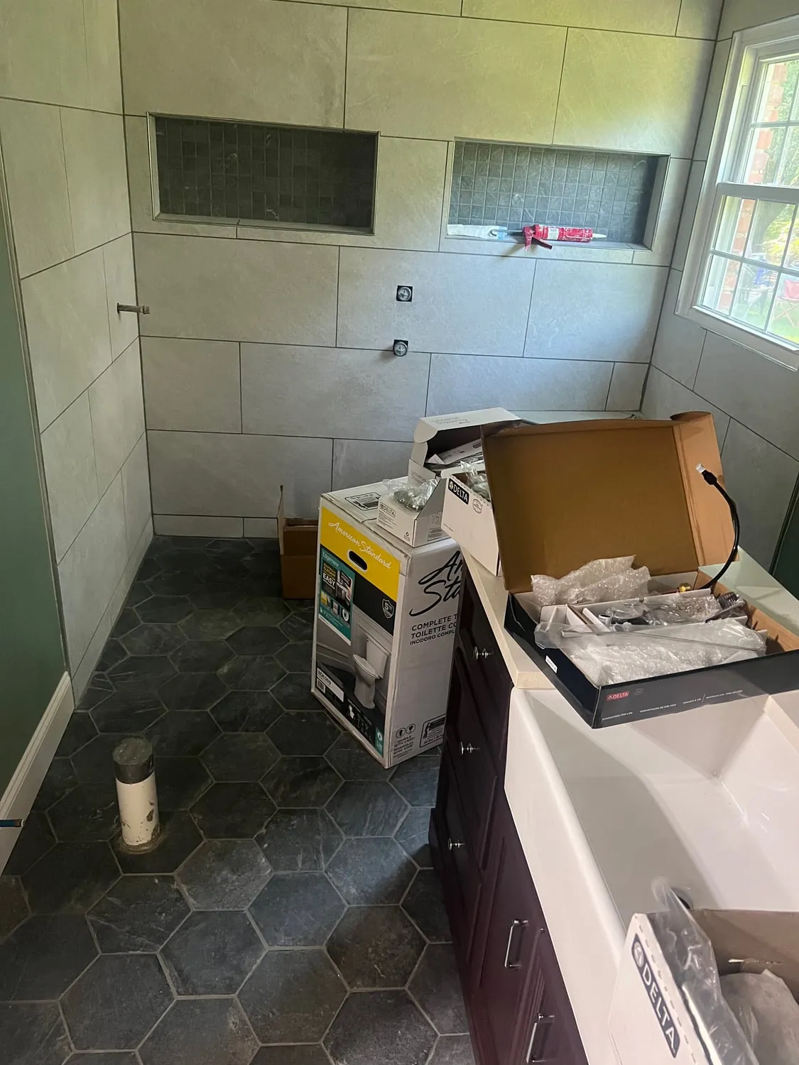 Bathroom mid-remodel with shower niches tiled, a vanity in place and fixtures still boxed