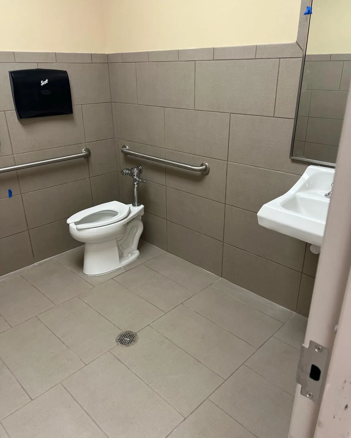 Commercial restroom with a flush-valve toilet, grab bars and a wall-hung sink