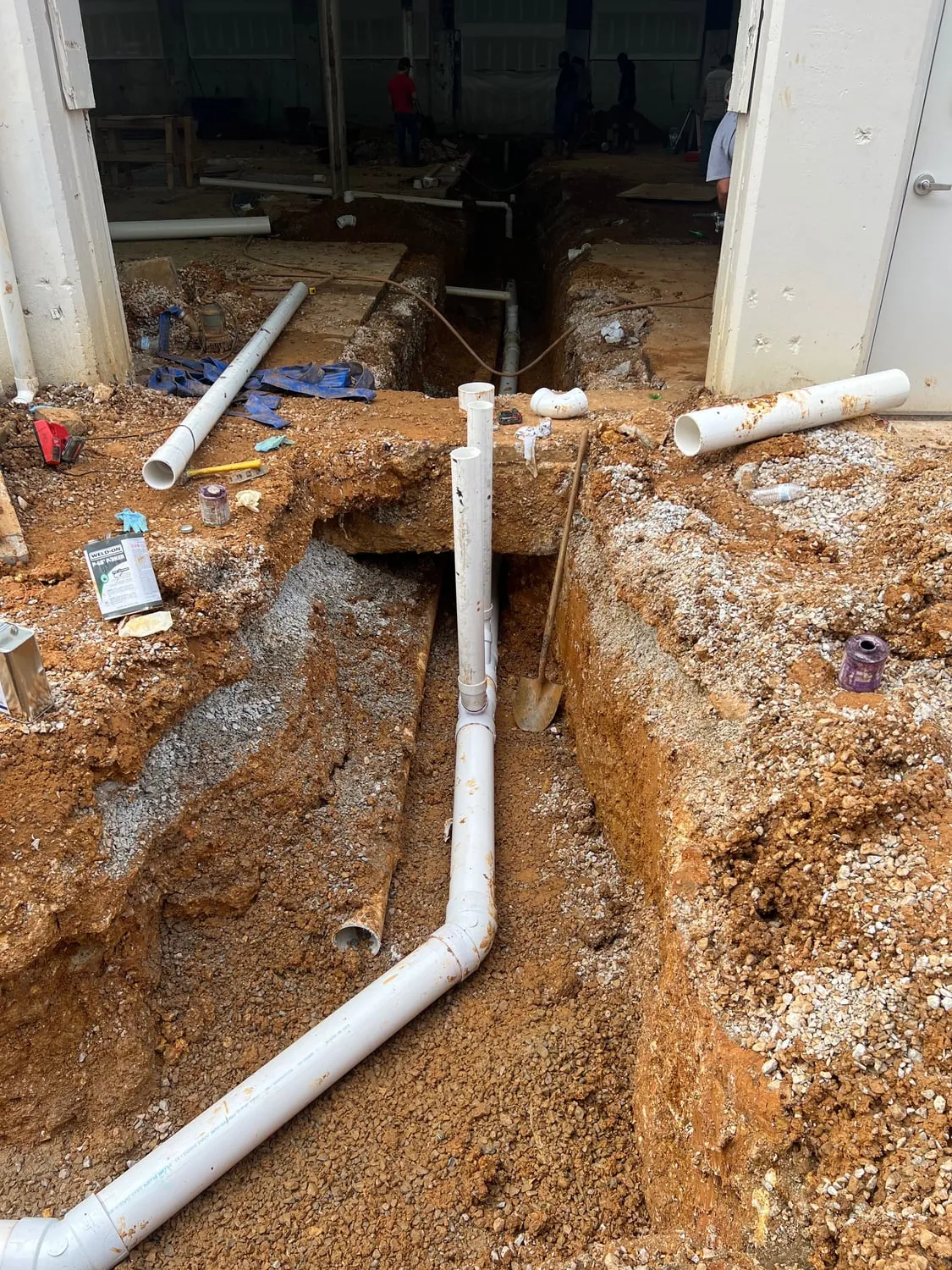 White PVC drain line laid in a trench cut through a building's floor slab