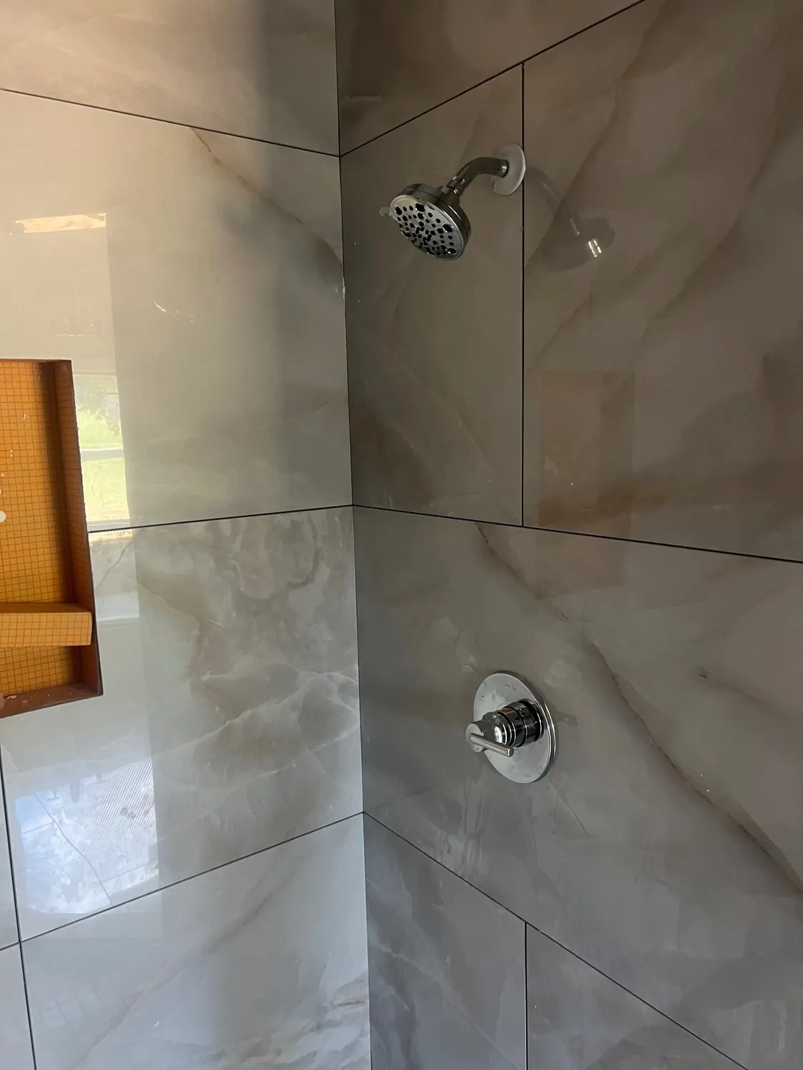 Chrome shower valve trim and shower head in large marble-look tile