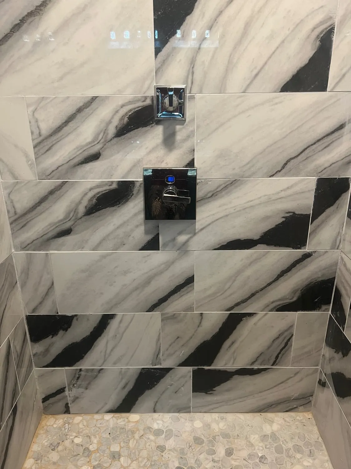 Shower with marble-look wall tile, a digital control and a pebble tile floor
