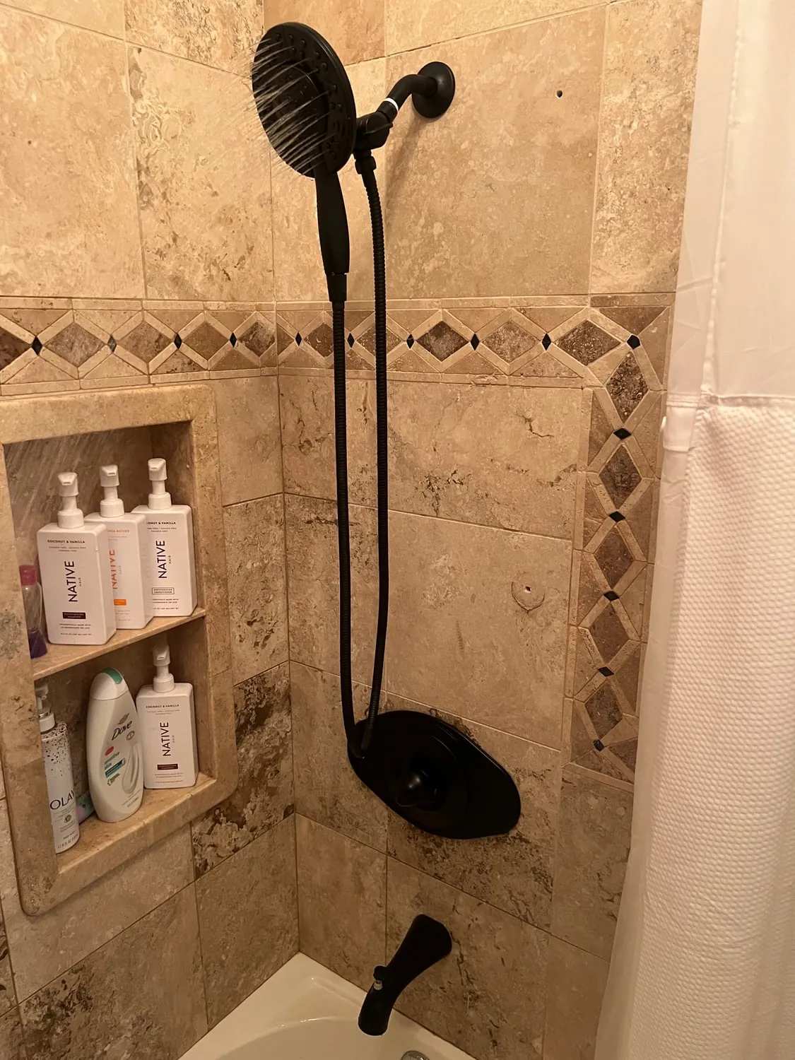 Matte black handheld shower and valve trim in a travertine tub surround