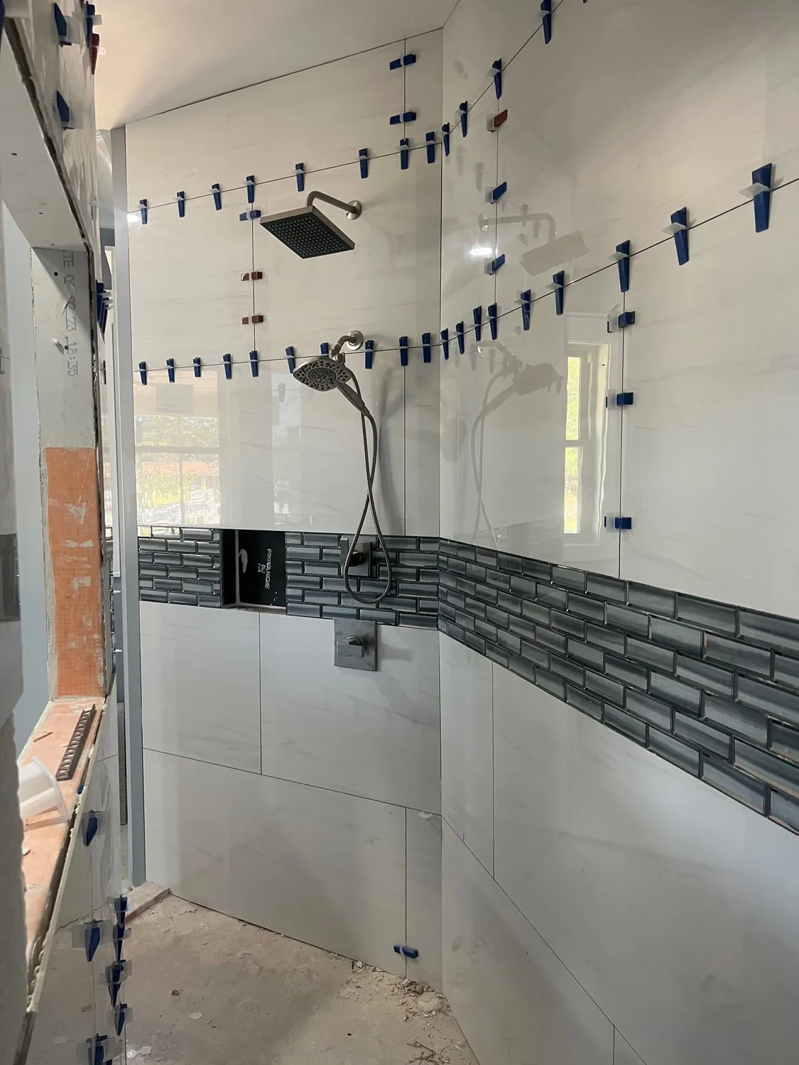 Shower valve, rain head and handheld set in a wall while tile goes up with leveling clips