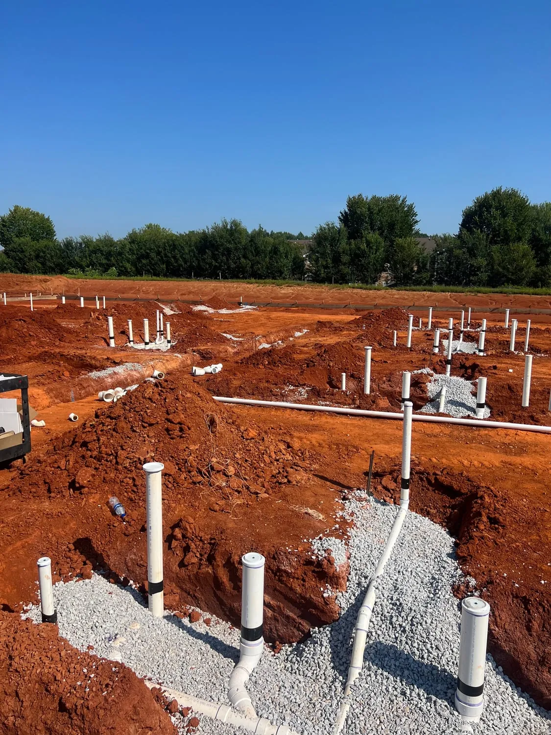 Rows of plumbing stub-ups across a red clay building site under a blue sky