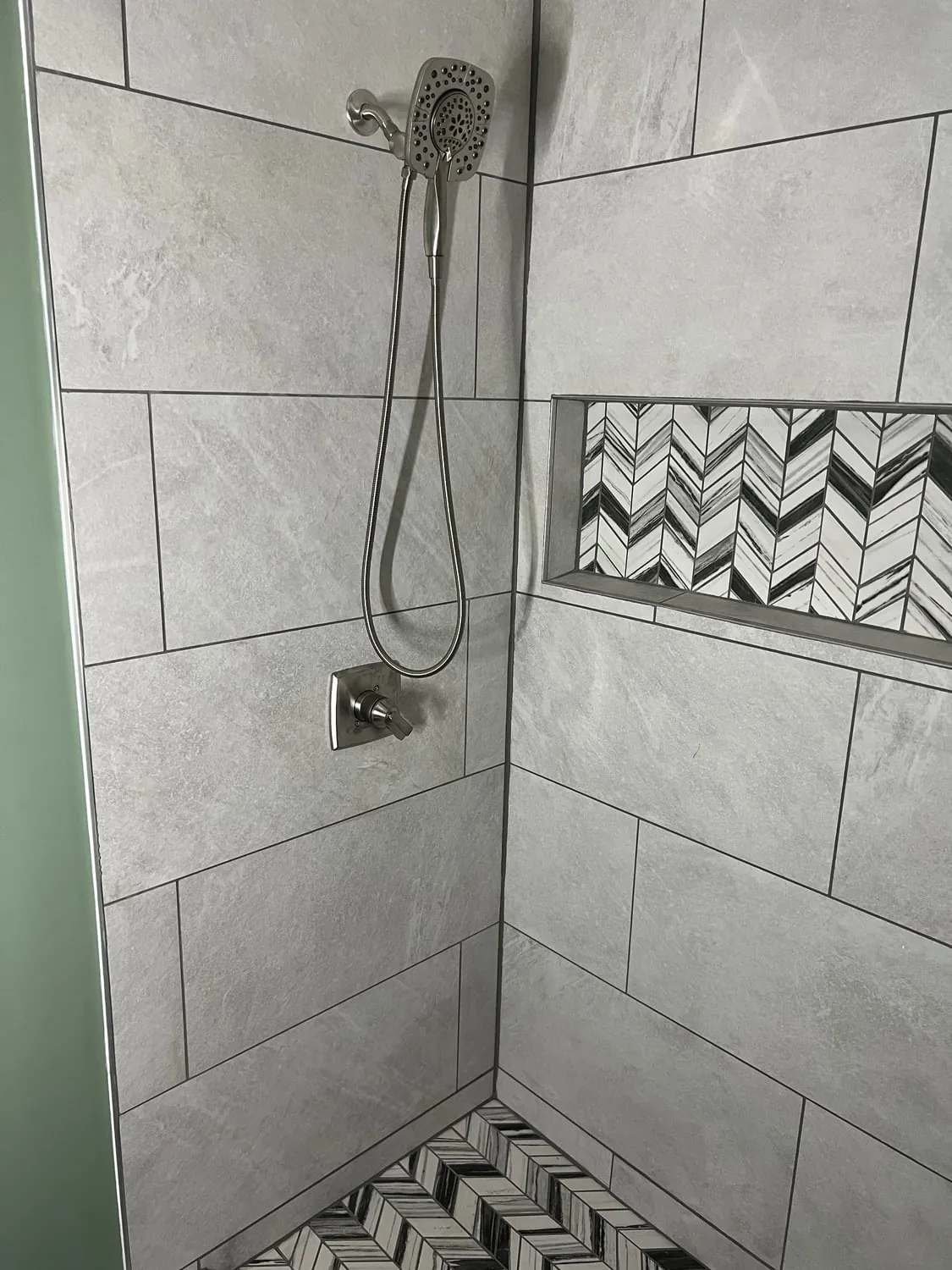 Tiled shower with a handheld shower and a herringbone tile niche