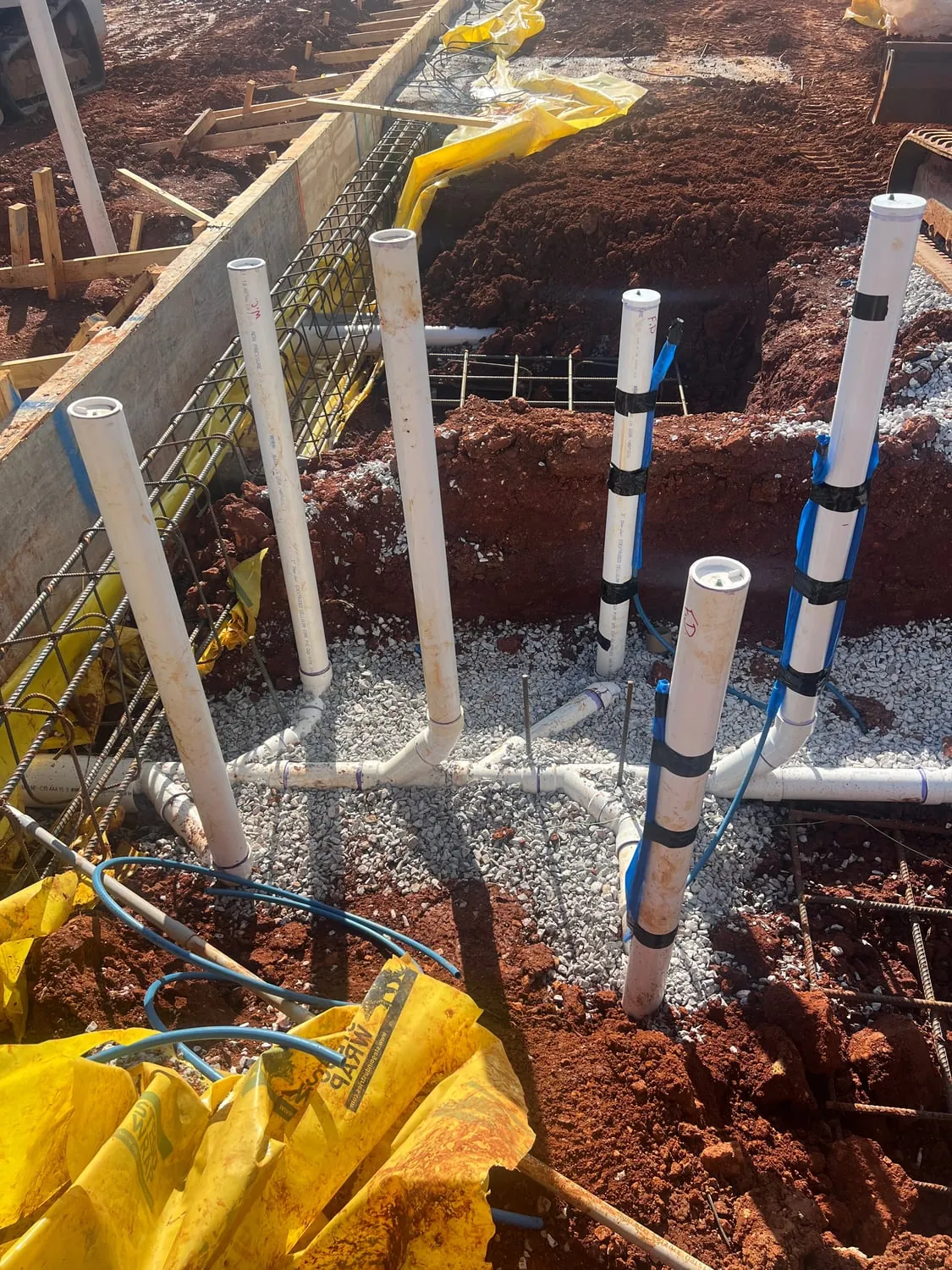 PVC stub-ups and supply lines set inside foundation forms with rebar and red clay