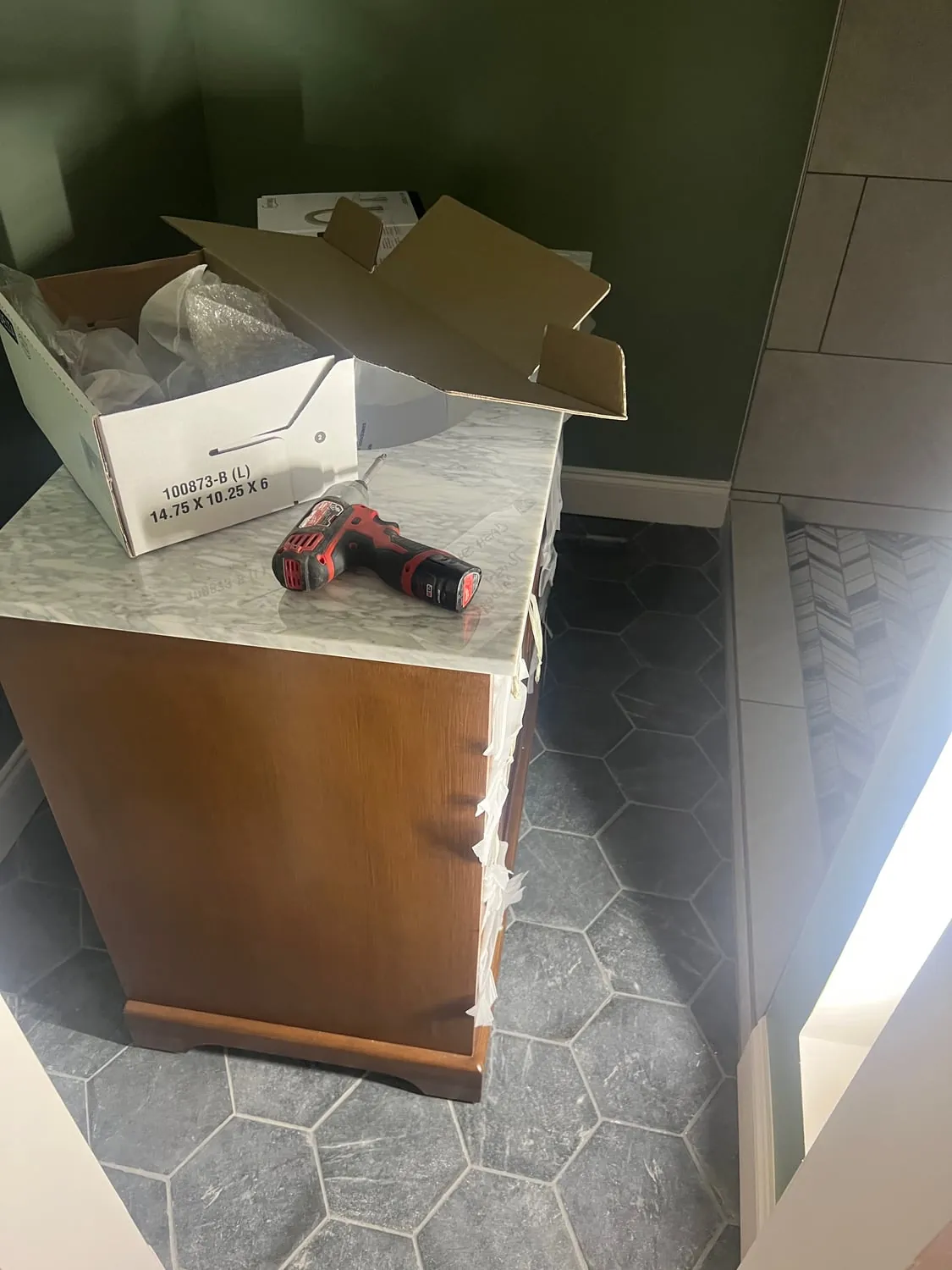 Bathroom vanity being installed on a hex tile floor with boxes and a drill on top