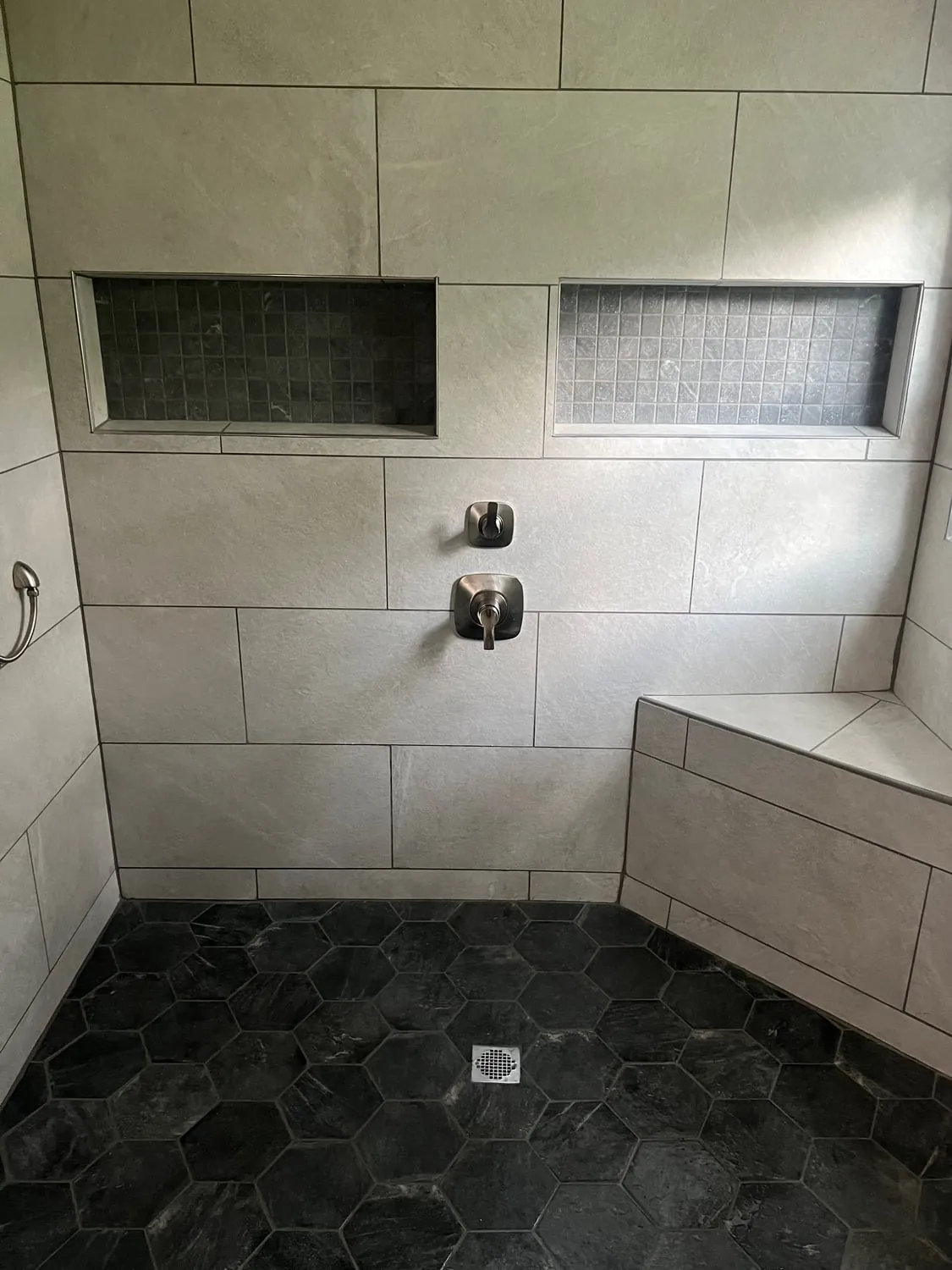 Finished walk-in shower with a tiled bench, two niches and a black hex tile floor